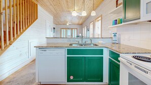 Una cocina moderna con techo de madera, encimeras de granito, lavavajillas, estufa y armarios verdes.
