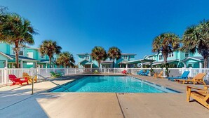 Una piscina con sillas de descanso, una cerca de piquetes blancos y edificios turquesa.