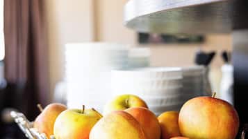 Una cesta de frutas sobre una mesa, con una pila de platos al fondo.