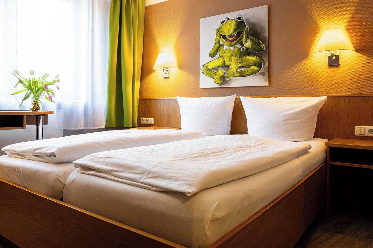 A hotel room with two beds, a painting of a frog, and two bedside lamps.