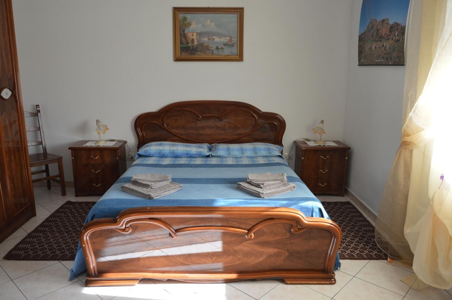 Una camera da letto con un letto in legno, due comodini, una sedia e due quadri appesi al muro.