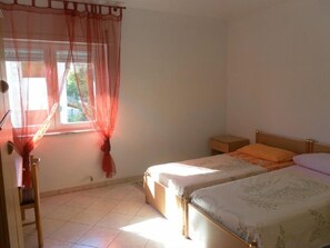 Un dormitorio con dos camas individuales, una mesita de noche, una silla y una ventana con cortinas de encaje.
