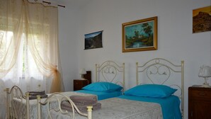 Une chambre avec deux lits simples, une table de chevet, une lampe et une fenêtre avec des rideaux légers.