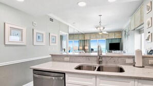 A modern kitchen with a large island, stainless steel appliances, and a view of the balcony. - Seawind 1309 | Updated condo with perfect beach view and walk to dine, shop, more! (Gulf Shores)