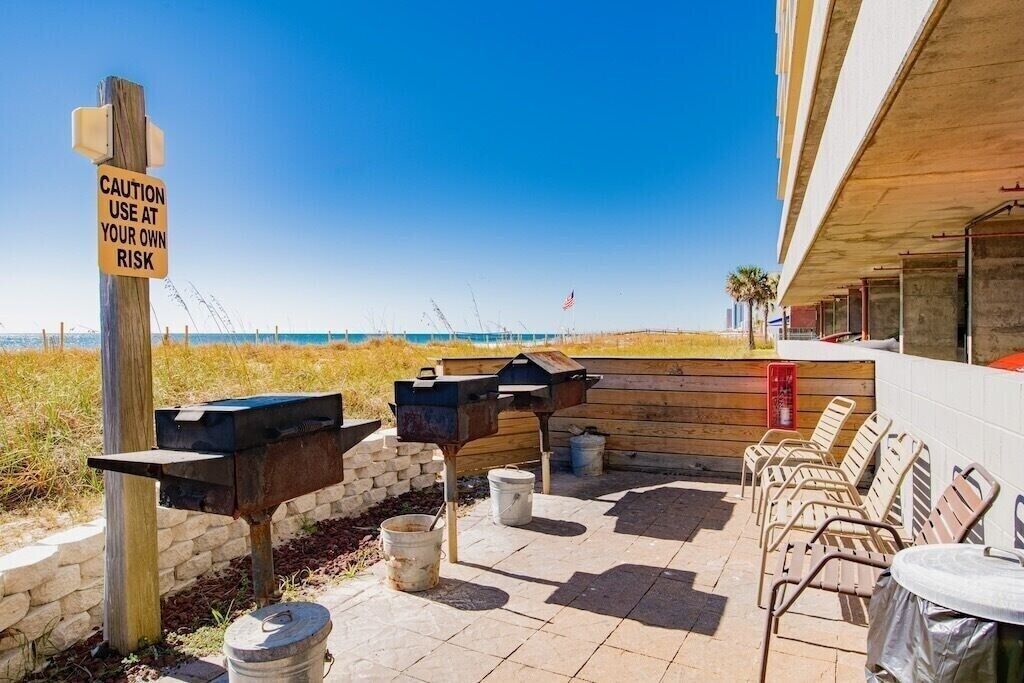 Une terrasse extérieure équipée de barbecues, agrémentée d’un panneau d’avertissement et offrant une vue sur la plage.