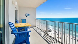 A balcony with a table and chairs, a dolphin mural, and a view of the beach and ocean. - Seawind 1309 | Updated condo with perfect beach view and walk to dine, shop, more! (Gulf Shores)