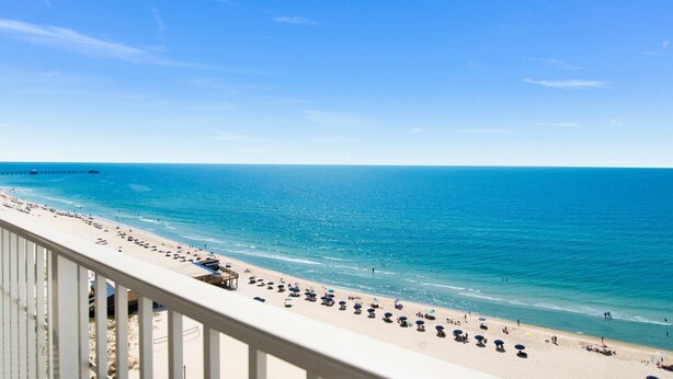 A beach with a long stretch of sand, a pier in the distance, and a clear blue sky. - Seawind 1309 | Updated condo with perfect beach view and walk to dine, shop, more! (Gulf Shores)