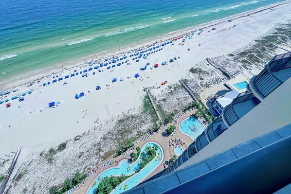 A beach resort with a swimming pool, beach umbrellas, and a boardwalk.