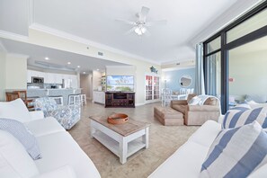 A spacious living room with a TV, white sofas, a coffee table, and a dining area with chairs.
