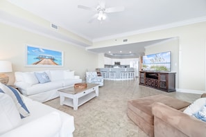A spacious living room with a white sofa, a coffee table, a TV, and a kitchen area with a bar.