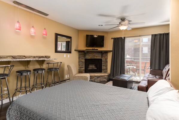 Una habitación de hotel con cama, chimenea, televisor, balcón con vistas y tres taburetes de bar.