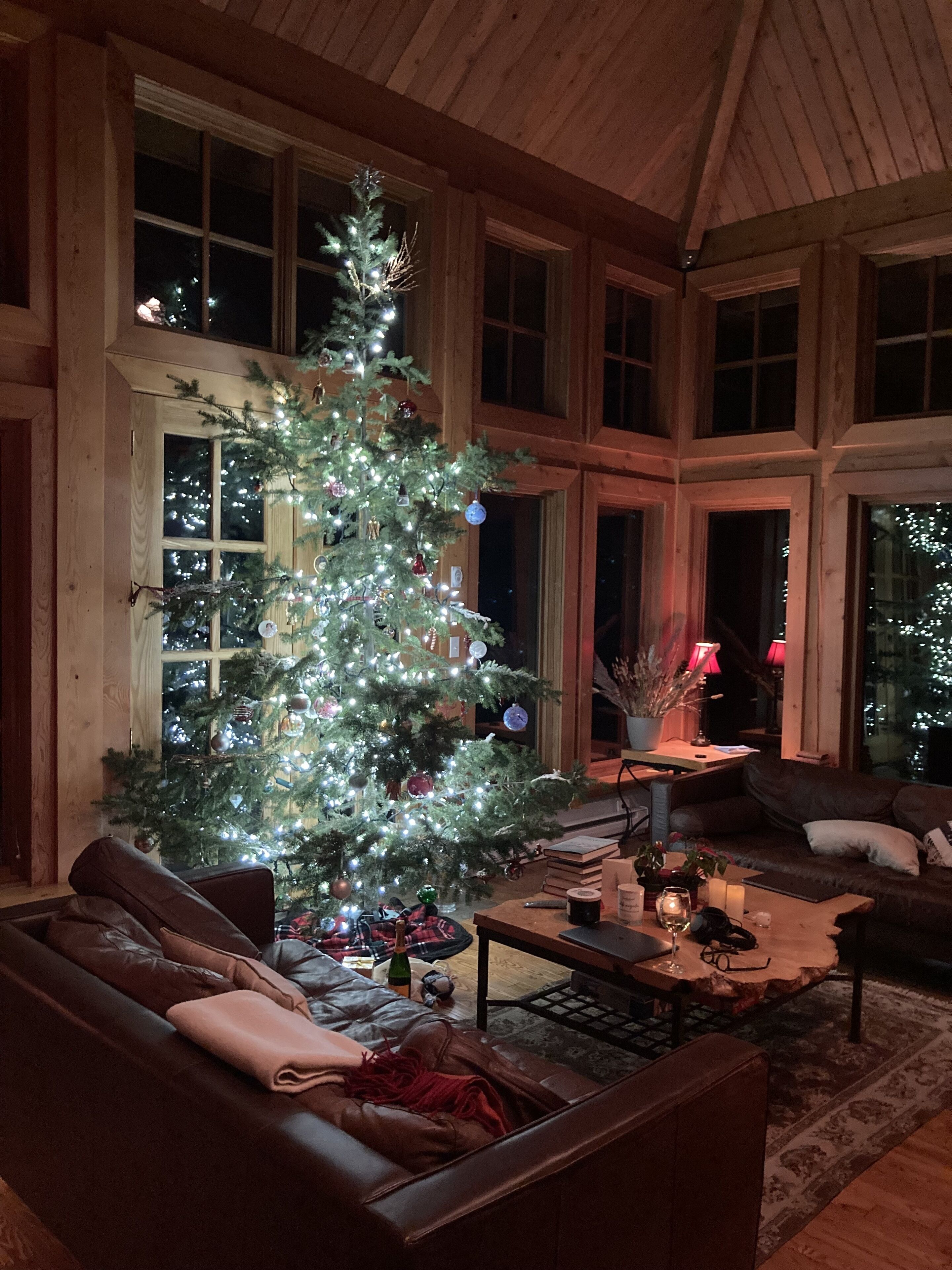 Un salon chaleureux avec un grand sapin de Noël, des murs en bois et un canapé en cuir.
