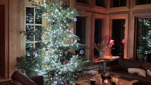 Un salón acogedor con un gran árbol de Navidad, paredes de madera y un sofá de cuero.