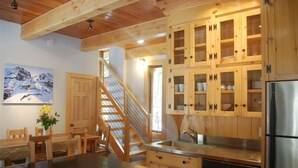 Un interior de madera con cocina, armarios de madera, una mesa de comedor, sillas y una escalera.