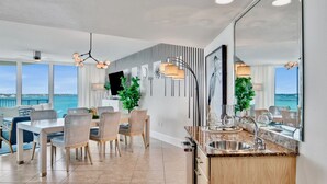Una cocina moderna con una isla grande, un comedor con sillas de mimbre y vista al océano.