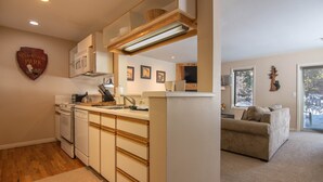 Een moderne keuken met witte apparaten, houten kasten en een centraal eiland. Er is een zithoek met een bank en een groot raam.