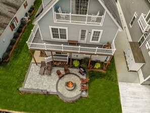 A two-story house with a covered patio area featuring a circular fire pit and outdoor seating. - Upscale Waterfront Home with Elevator, Solar Powered (Selbyville)