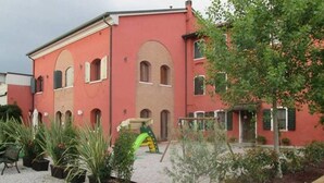 Un bâtiment rouge doté de fenêtres en arc de cercle et d’un petit jardin agrémenté de plantes en pot.