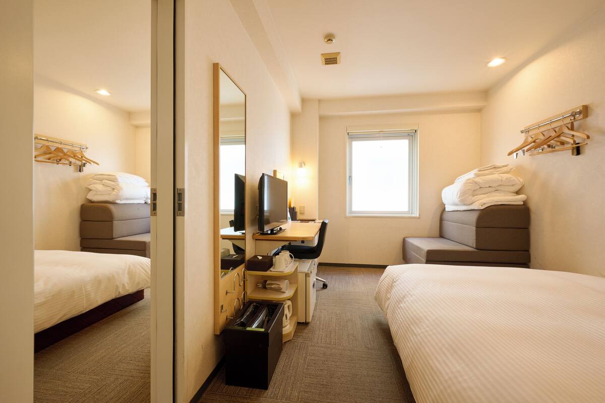 Een hotelkamer met twee bedden, een bureau, een televisie en een raam.