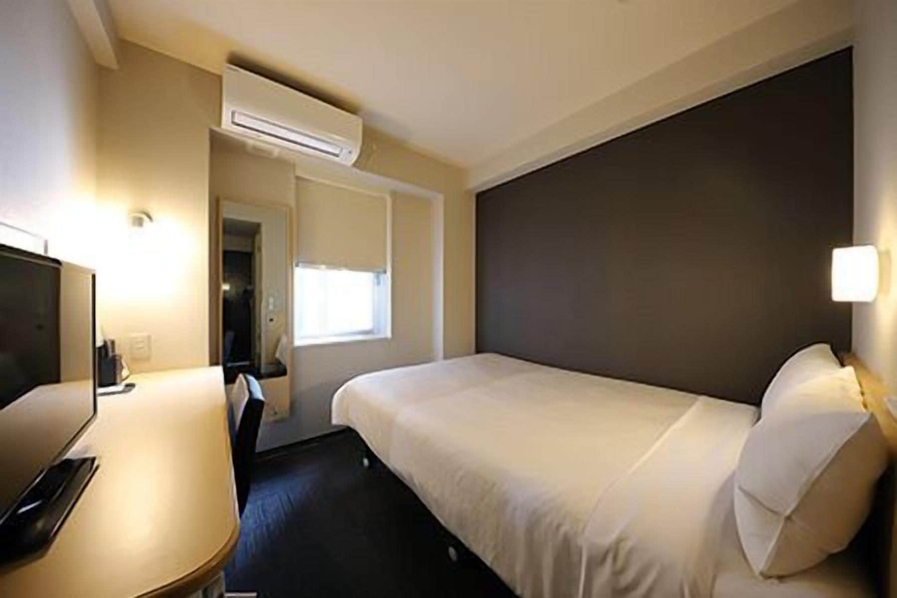 Ein Hotelzimmer mit Bett, Schreibtisch, Stuhl, Klimaanlage und Fenster.
