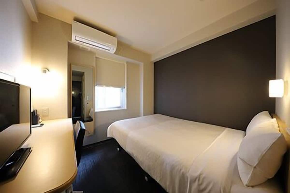 Een hotelkamer met een bed, een bureau, een stoel, een airconditioning en een raam.