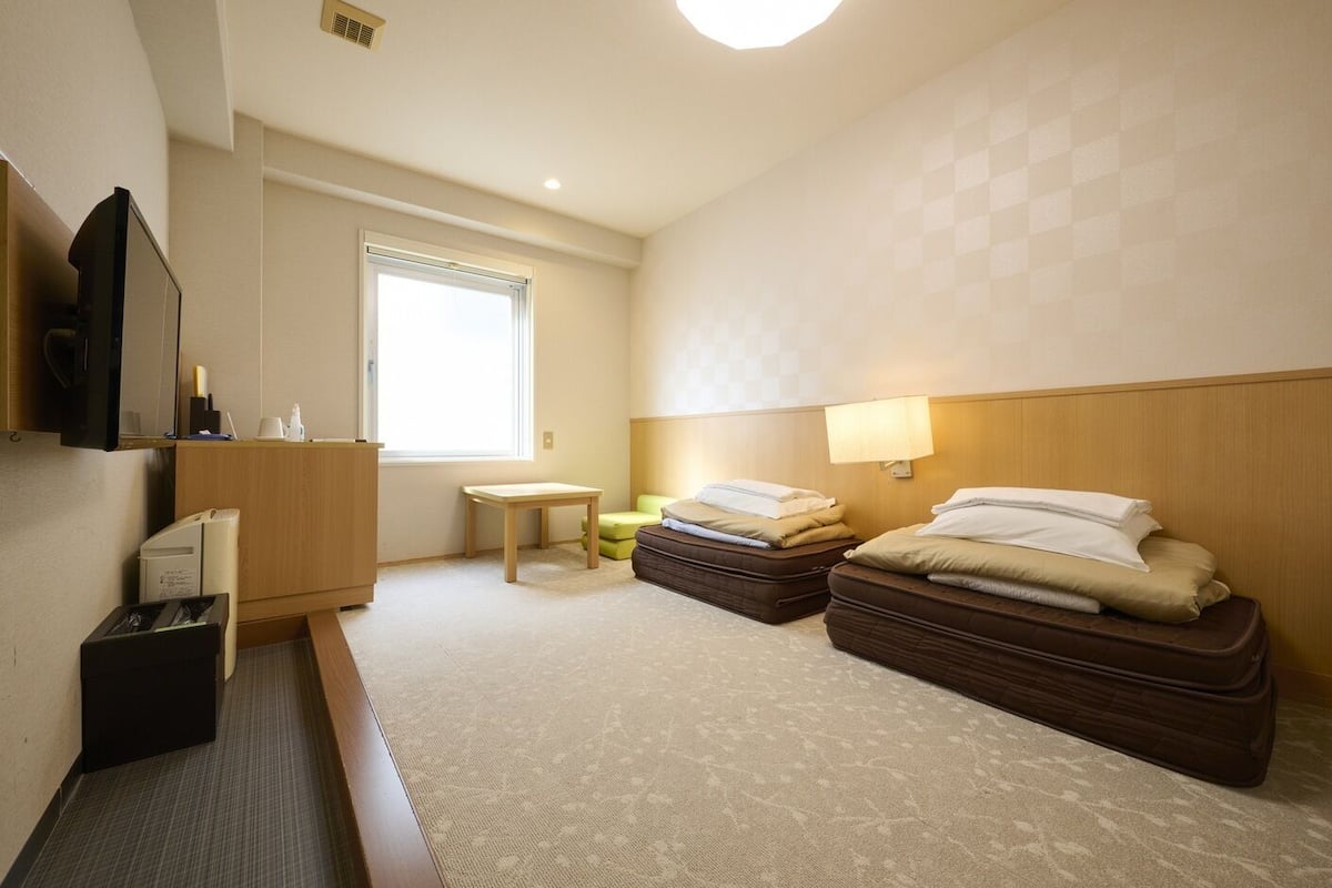 Une chambre d’hôtel avec deux lits, un bureau, une chaise, une télévision et une fenêtre.