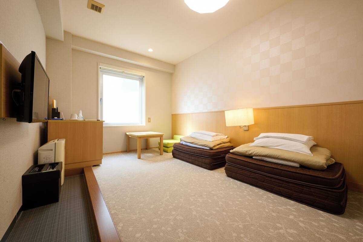 Een hotelkamer met een bed, een bureau, een stoel, een klein tafeltje, een raam en een aan de muur bevestigde televisie.
