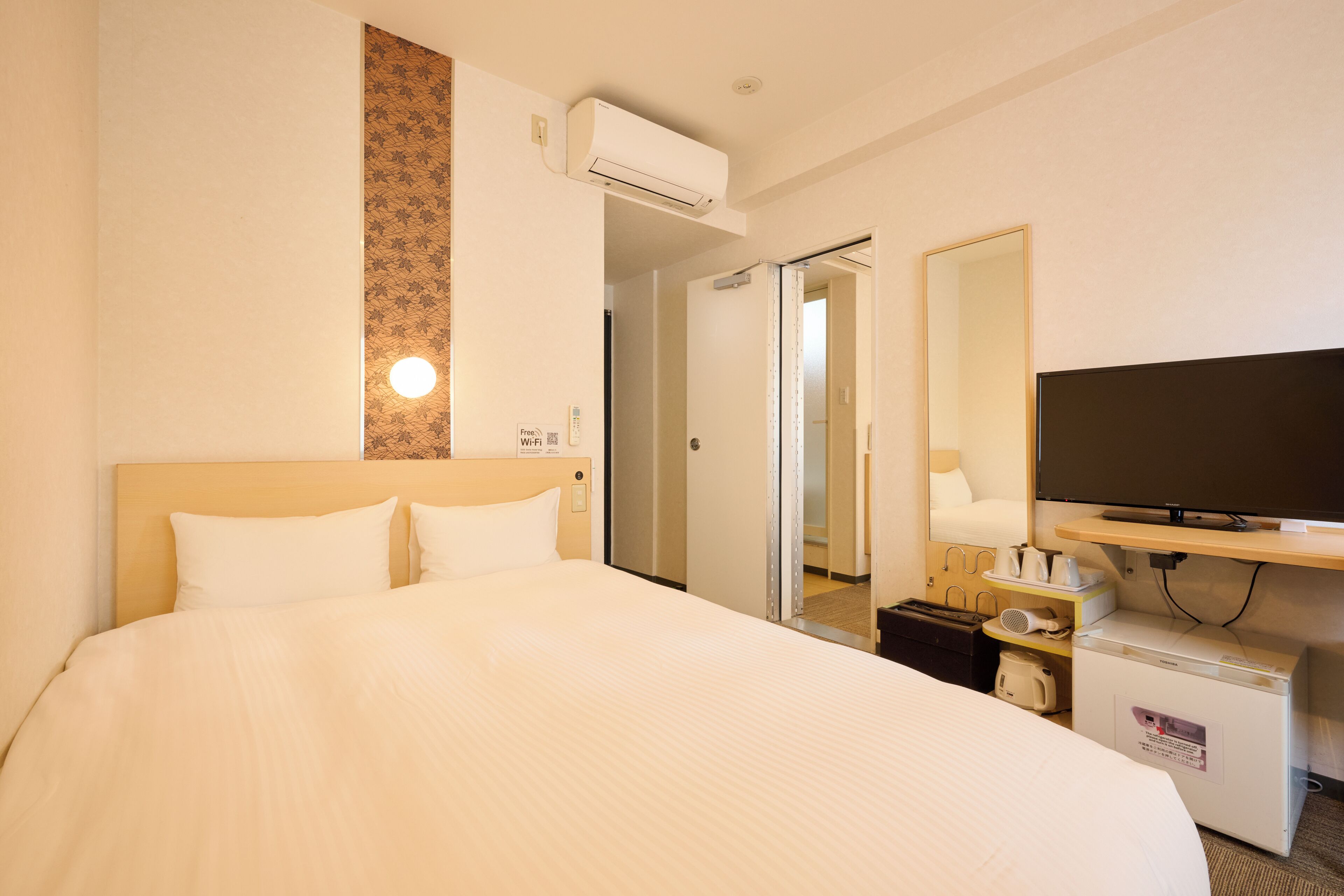 Una habitación de hotel con una cama grande, un televisor de pantalla plana, un escritorio pequeño con una lámpara y un equipo de aire acondicionado.