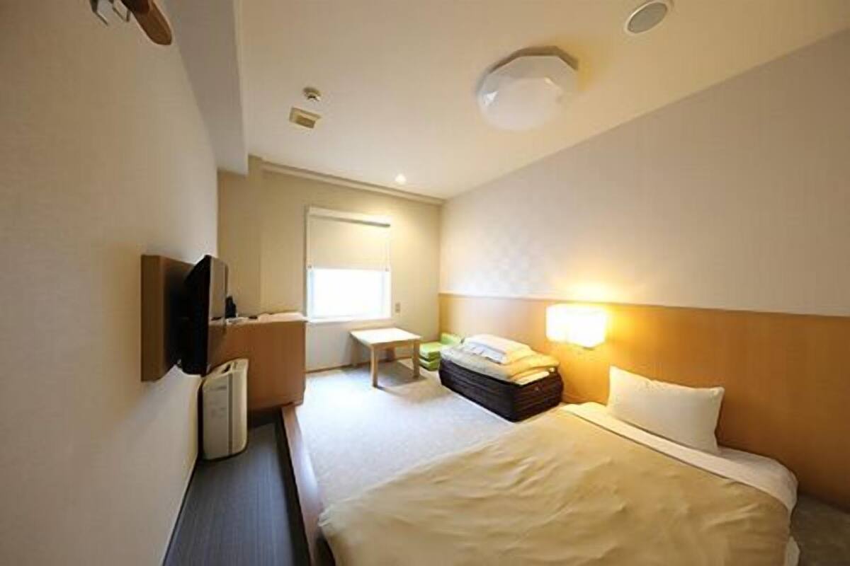Een hotelkamer met een bed, nachtkastje, lamp en een televisie.