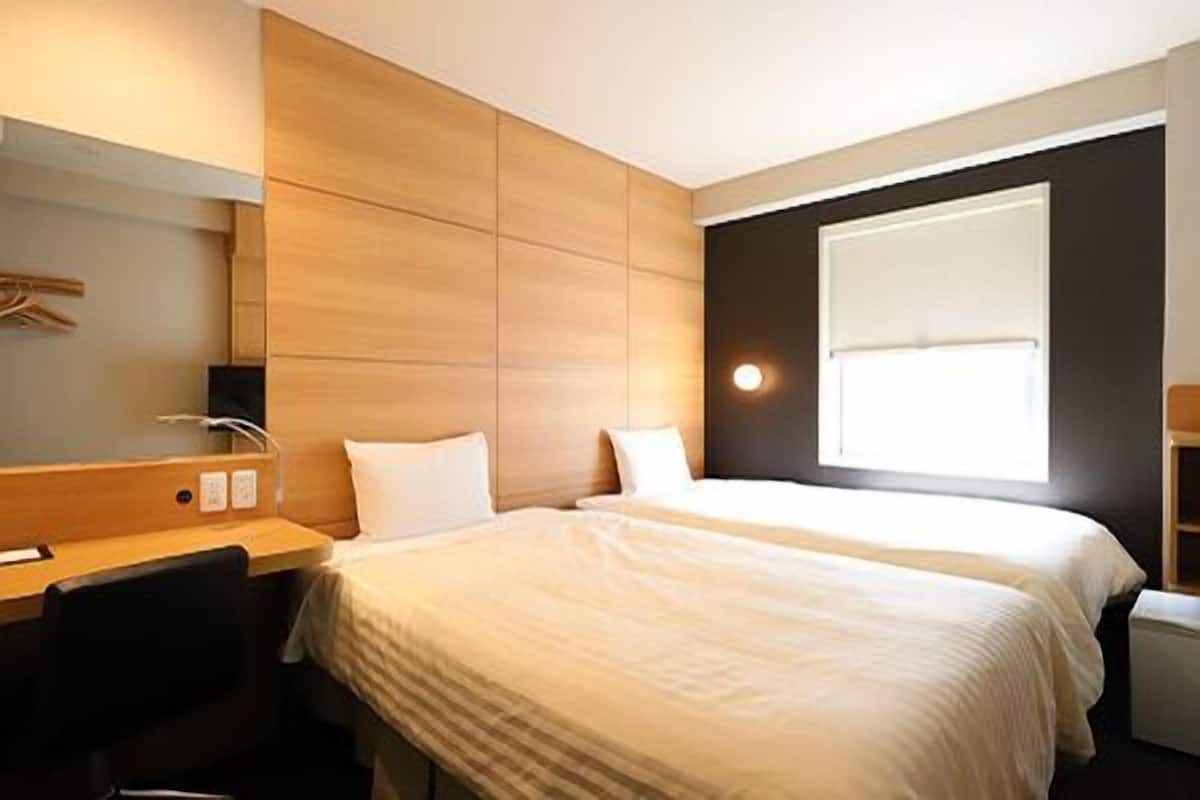 Een hotelkamer met twee bedden, een bureau, een stoel, een spiegel en een raam.