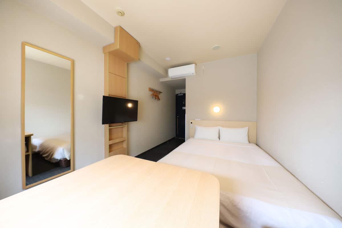 Een hotelkamer met twee bedden, een televisie, een spiegel en een kledingkast.