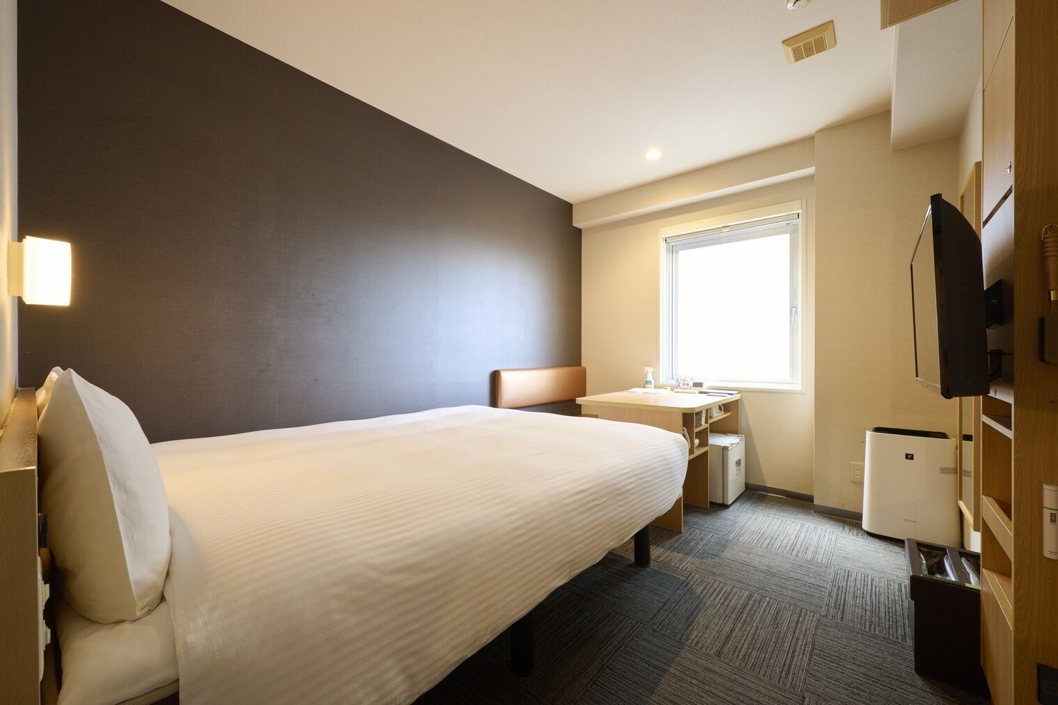 Ein Hotelzimmer mit Bett, Schreibtisch, Stuhl, Fenster und Fernseher.