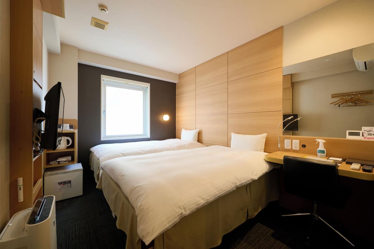 Een hotelkamer met een groot bed, een bureau met stoel, een televisie, een magnetron en een raam dat voor daglicht zorgt.