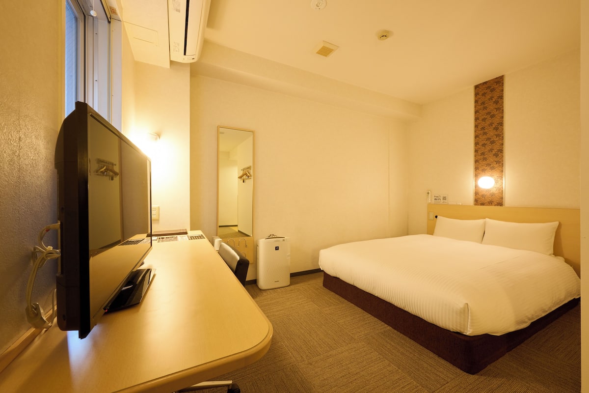 Hotelkamer met een bed, een bureau met een computer, een spiegel en een wandlamp.
