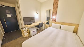 A hotel room with a bed, desk, chair, and a small refrigerator.