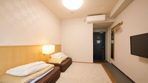 Una habitación de hotel con dos camas, un televisor montado en la pared y un equipo de aire acondicionado.