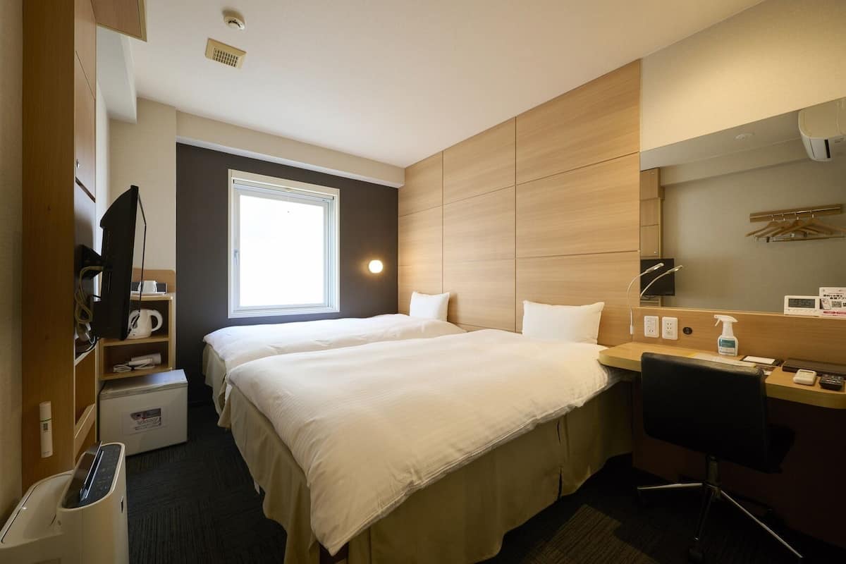 Une chambre d’hôtel avec deux lits, un bureau, une chaise, une télévision, une machine à café, un radiateur et une fenêtre.