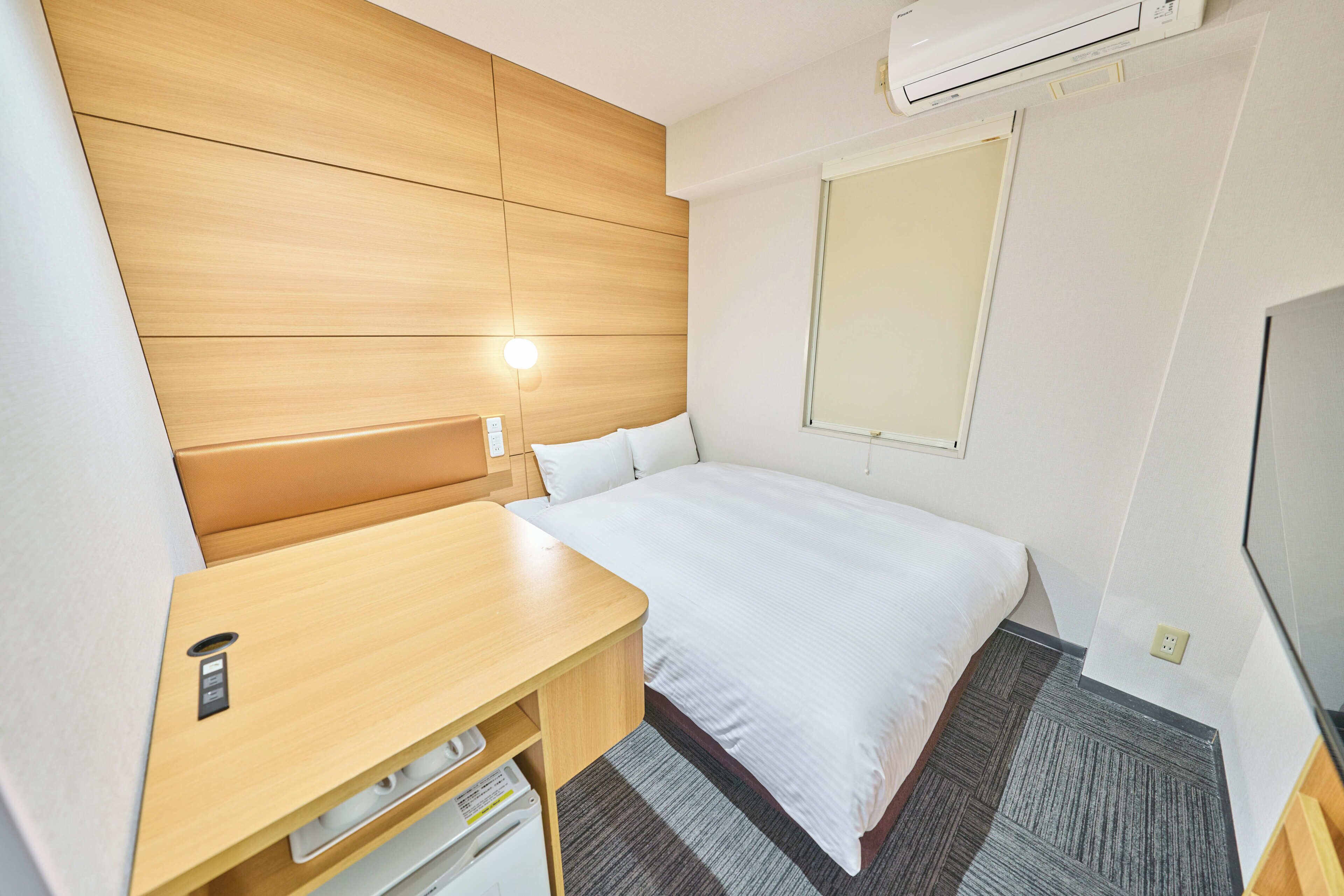 Een hotelkamer met een houten hoofdbord, een enkel bed, een nachtkastje met een lamp en een klein bureau met een printer.