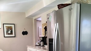 A kitchen with a stainless steel refrigerator, white cabinetry, a marble countertop, and a framed picture on the wall.