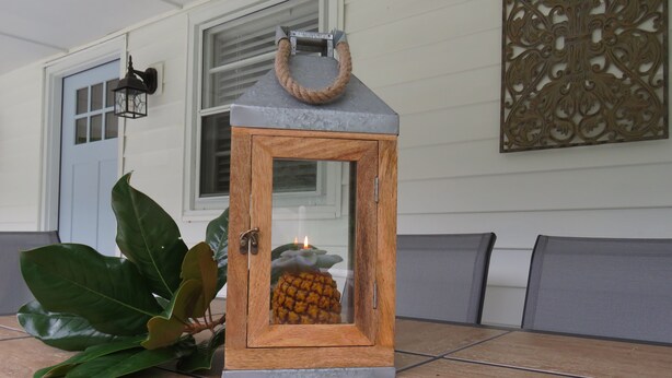 A wooden lantern with a rope handle on a tiled patio.