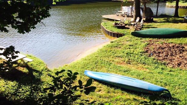 Terraza junto al lago con un bote, una zona de estar cubierta y una orilla con césped.