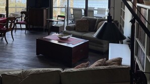 Amplia sala de estar con ventanas grandes, un sofá acogedor, una zona de comedor y una escalera.