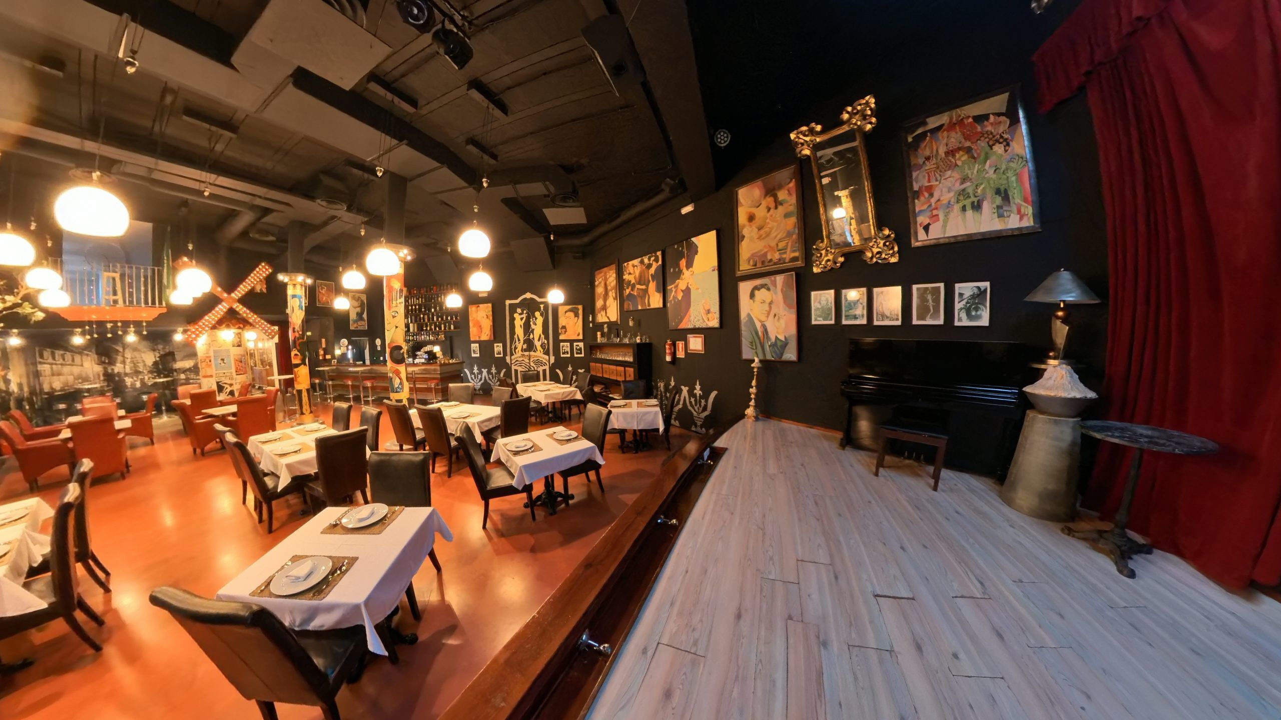 A restaurant with tables set for dining, a piano, and artwork on the walls.