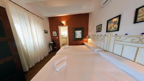 Habitación de hotel con dos camas, un escritorio, una silla, un espejo y una pared decorada con cuadros.