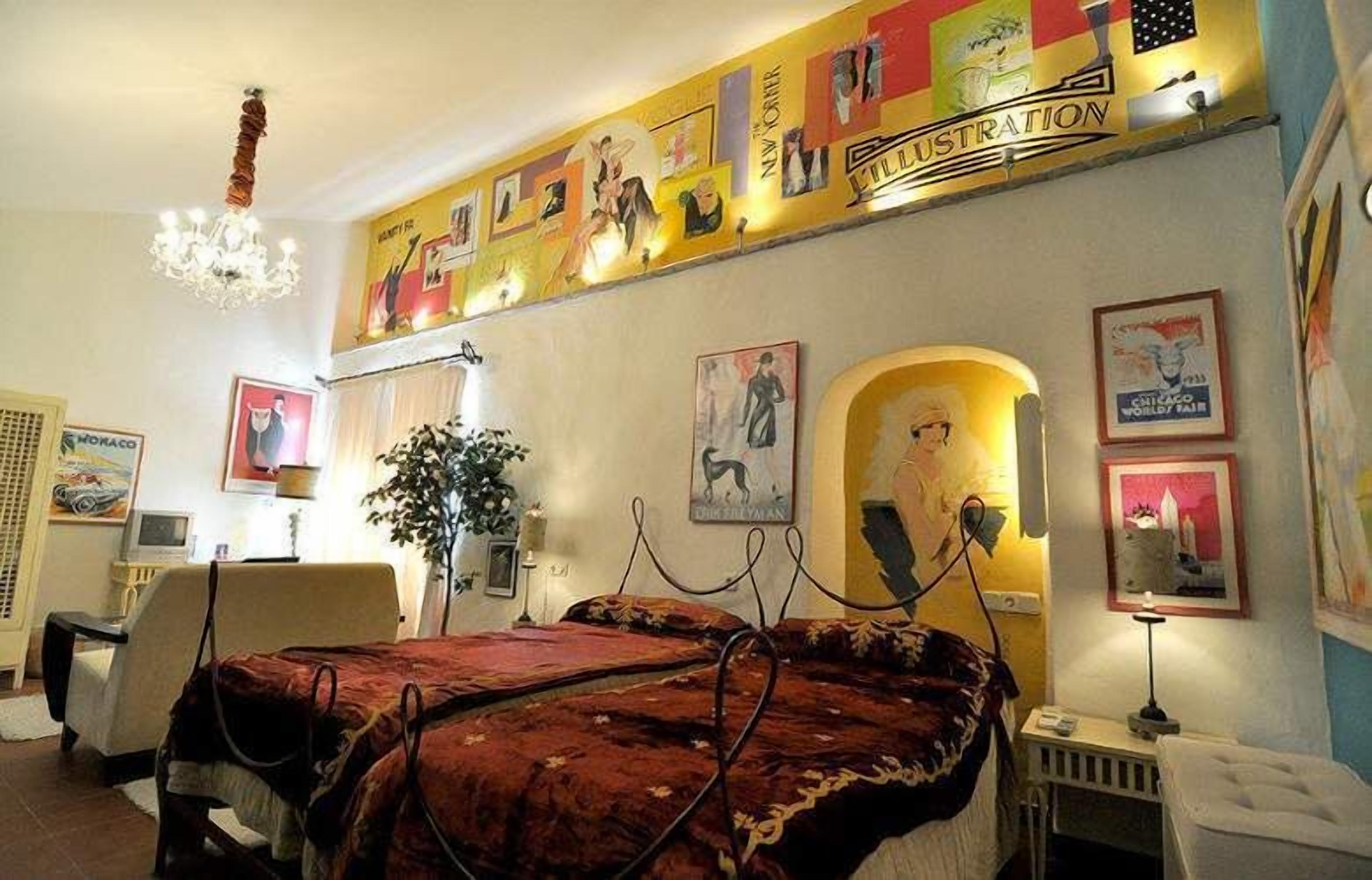 Habitación de hotel con una cama grande, un escritorio, una silla, una planta y obras de arte en las paredes.