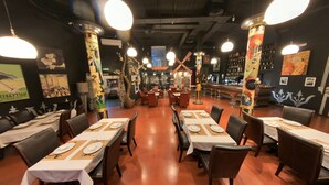 Un restaurante con mesas dispuestas para comer, una zona de bar y pilares decorativos.