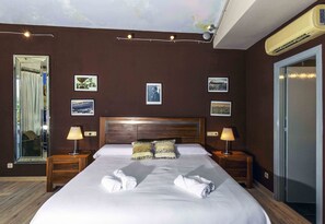 Een hotelkamer met een groot bed, twee nachtkastjes met lampen, een plafondlamp en ingekaderde foto’s aan de muur.