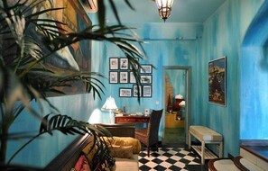 A room with a checkered floor, a desk with a lamp, a chair, and framed pictures on the wall. - Hotel Utopía (Benalup-Casas Vieja)