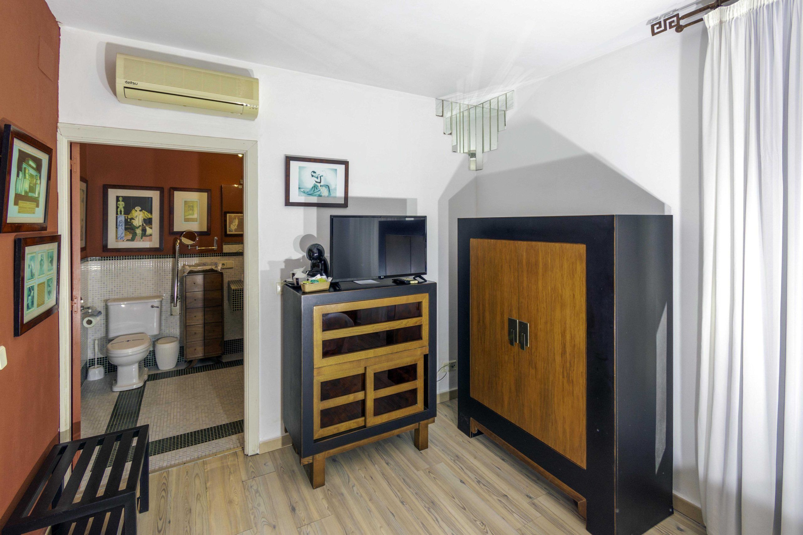 Une chambre d’hôtel compacte comprenant un meuble en bois, une télévision, un miroir et un petit coin salon.