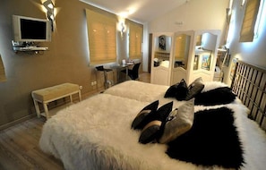 Quarto com uma cama grande, um banquinho, uma televisão e um espelho.